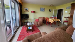 Una sala de estar con un sofá, una mesa de comedor con sillas, un televisor y una lámpara roja.