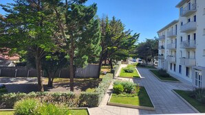 Un barrio residencial con un camino pavimentado, árboles y un edificio de varios pisos con balcones.