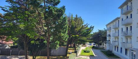 A residential area with a paved walkway, trees, and a multi-story building with balconies.