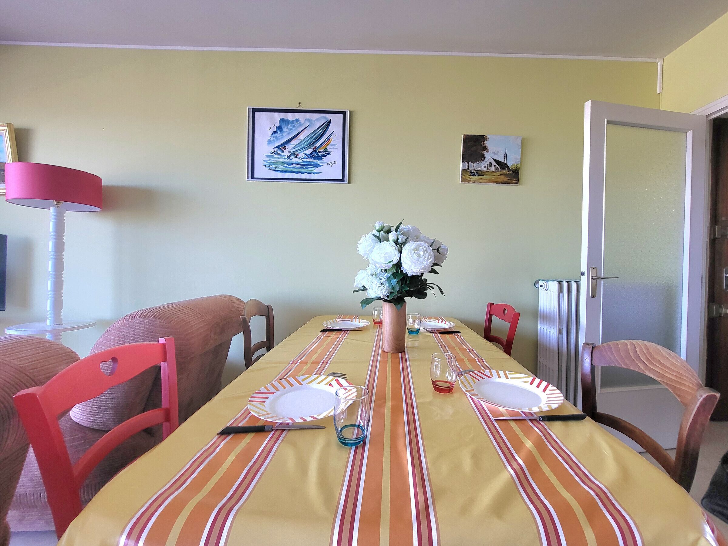 A dining room with a striped tablecloth, a vase of flowers, and two framed artworks on the wall.