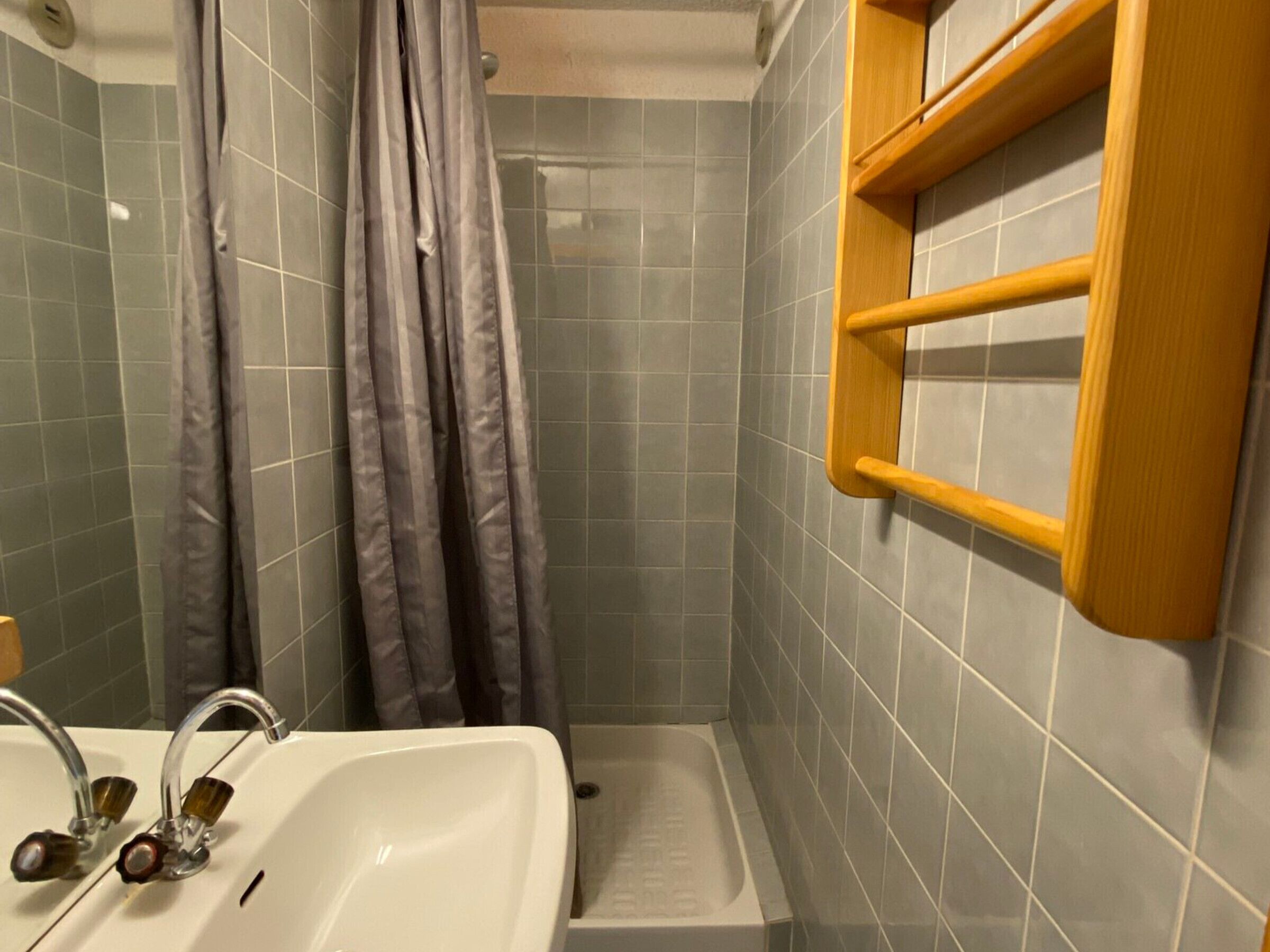 A bathroom with a white sink, a shower with a curtain, and a wooden shelf.