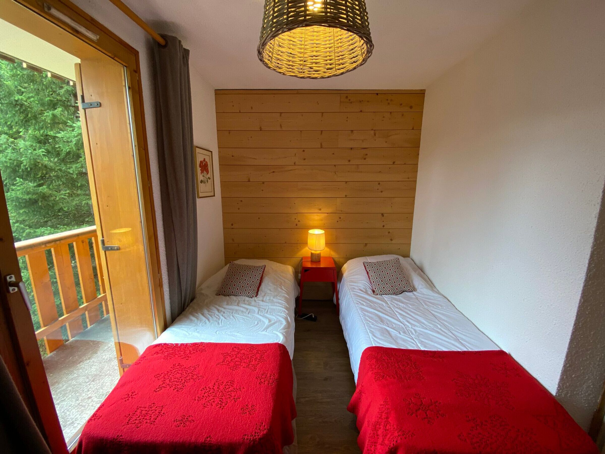 A room with two beds, a wooden wall, a window, and a door leading outside.