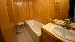 A wooden-paneled bathroom with a bathtub, a sink, and a small stool.
