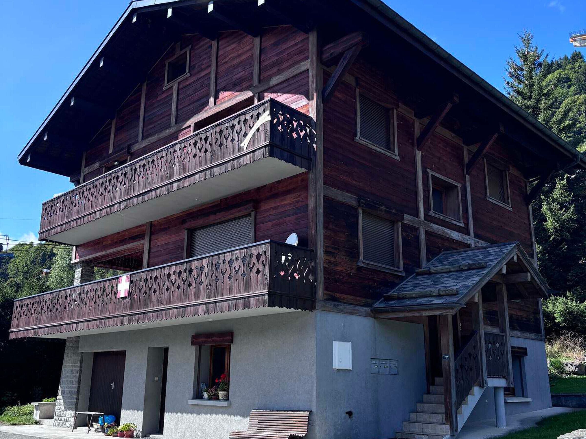 Ein zweistöckiges Holzhaus mit Balkonen, einem Steinsockel und einer kleinen Veranda.