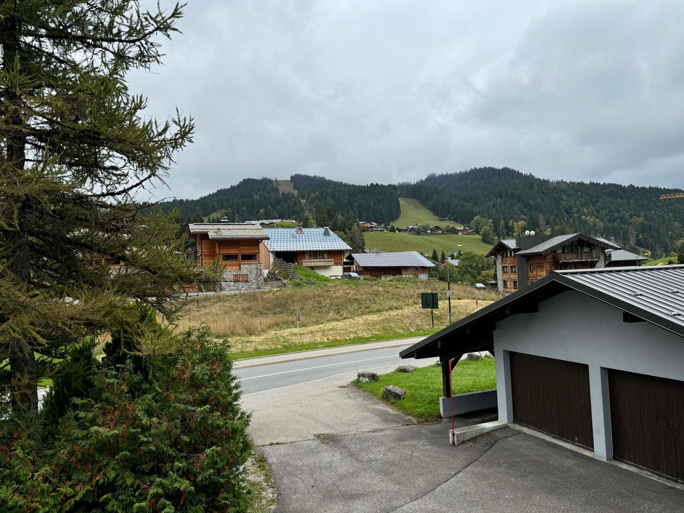 A mountain village with traditional wooden houses, a paved road, and a view of the surrounding hills.