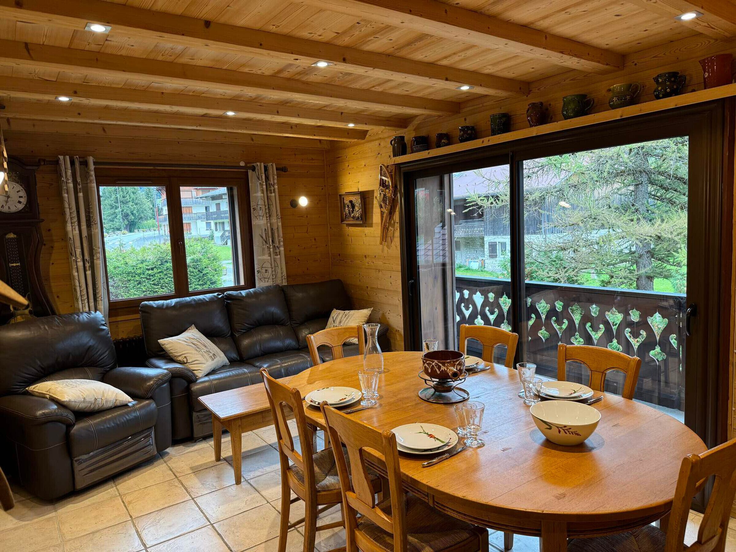 Une pièce chaleureuse avec un plafond en bois, un canapé en cuir, une table à manger avec des chaises et de grandes fenêtres donnant sur un paysage verdoyant.