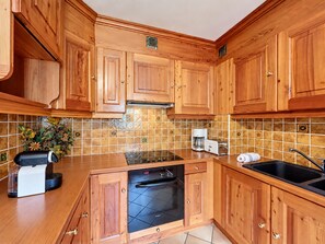 Een keuken met houten kastjes, een inbouwoven, een koffiezetapparaat en een spoelbak.