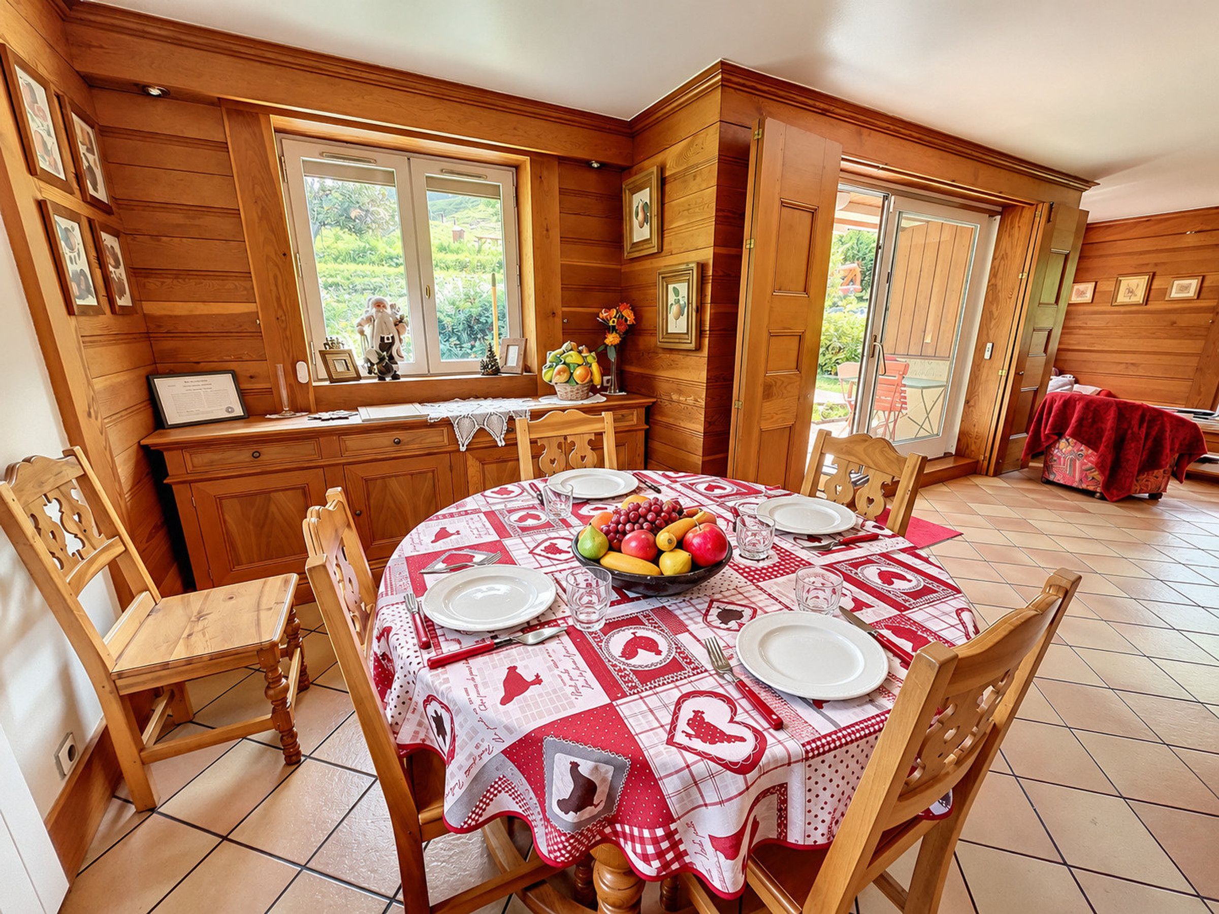 Ein Essbereich mit einem runden Tisch für vier Personen, Holzstühle und eine Küchenzeile mit Holzschränken und einem Fenster mit Blick auf einen Garten.
