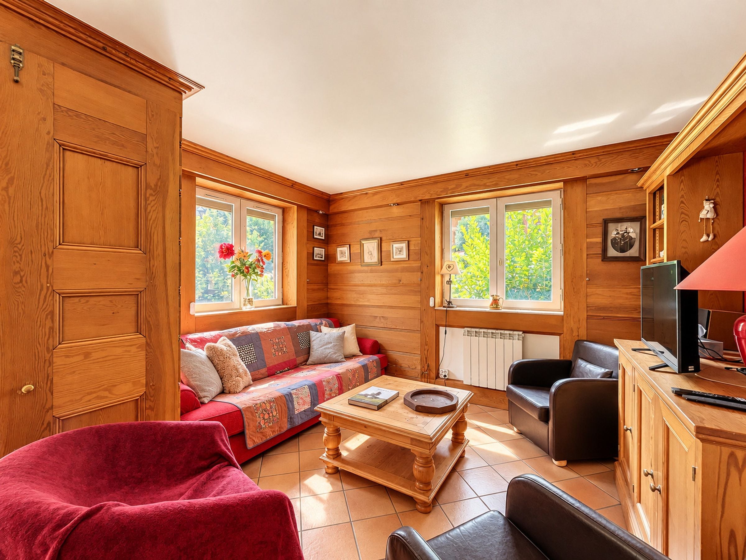 A cozy room with a wooden interior, a sofa, a red chair, a coffee table, and a television.
