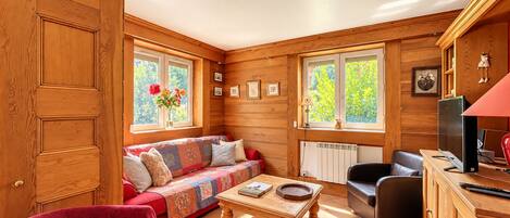 A cozy room with a wooden interior, a sofa, a red chair, a coffee table, and a television.