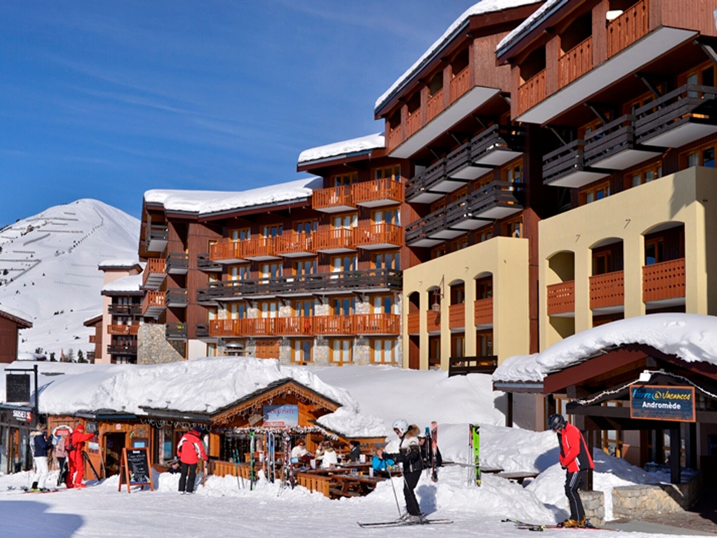 A ski resort with multi-story buildings, ski slopes, and a snow-covered mountain in the background.