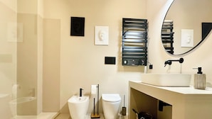 Une salle de bain moderne avec un lavabo blanc, des toilettes et un bidet. Un miroir est placé au-dessus du lavabo et un radiateur est fixé au mur.