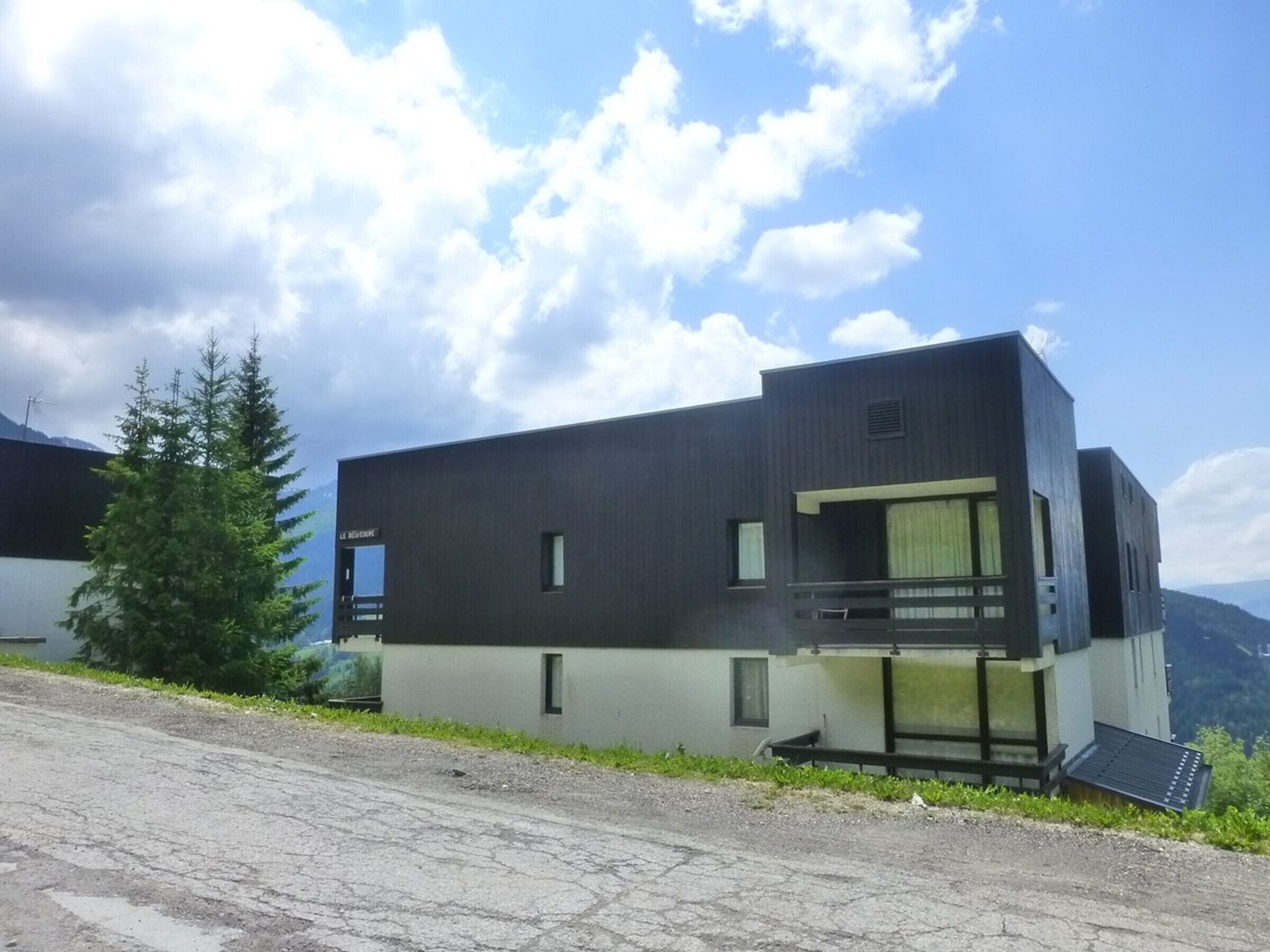 A modern two-story building with a flat roof, a balcony, and a small window.
