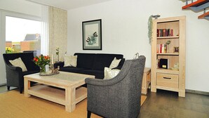Una sala de estar con un sofá negro, un sillón gris, una mesa de centro de madera y una estantería.