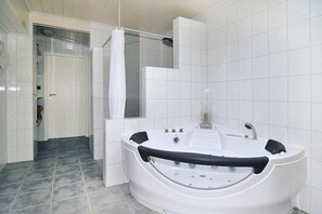 A modern bathroom with a large white bathtub, a shower area, and a door leading to another room. - Doppelhaushalfte, Friedrichskoog-spitze (Friedrichskoog)