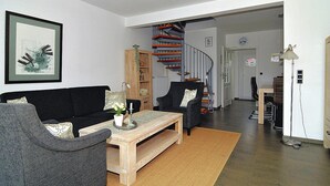 Una sala de estar con un sofá negro, una mesa de centro de madera y una escalera en espiral al fondo.