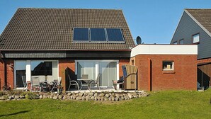 Una casa con techo inclinado, paneles solares, fachada de ladrillo y un patio con mobiliario exterior.