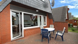 A house with a satellite dish, a large window with a heart-shaped decoration, and a patio with a table and chairs. - Ferienhaus Toms Hutte mit Terrasse in Dornum (Dornum)