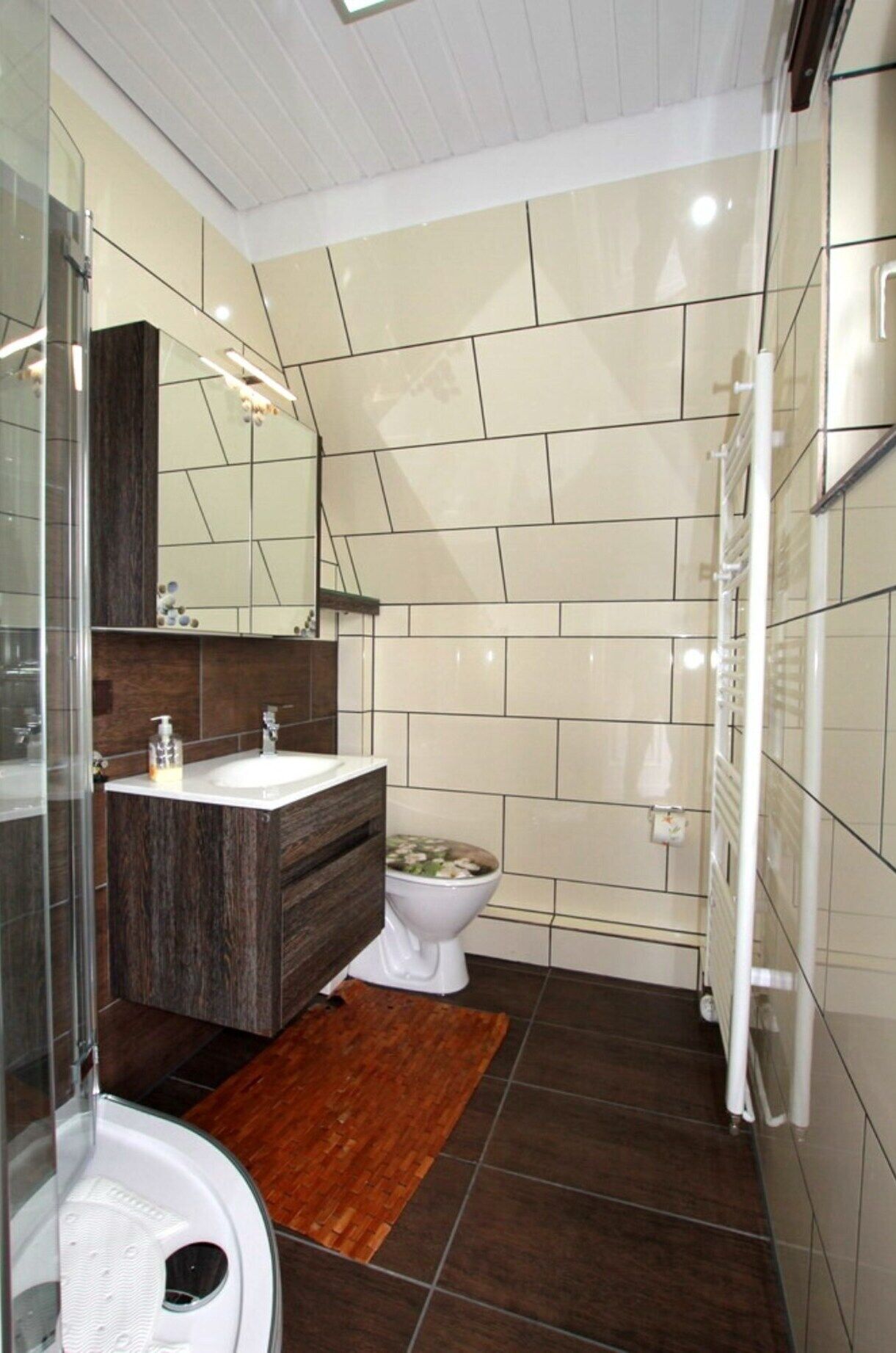 A modern bathroom with a glass shower enclosure, a wooden vanity, a white toilet, and a radiator.