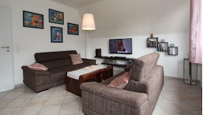 A living room with two brown sofas, a coffee table, and a television. There are framed pictures on the wall and a pink lamp. - Ferienhaus Toms Hutte mit Terrasse in Dornum (Dornum)