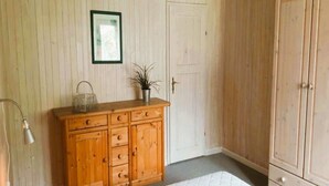 A bedroom with a wooden dresser, a bed with a quilt, a door, and a framed picture on the wall.