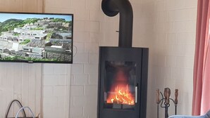 A modern living room with a black wood-burning stove, a television mounted on the wall, a grey sofa, and a grey bag on the floor.