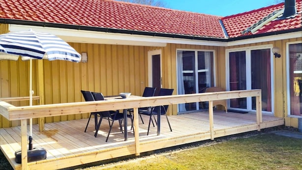 A wooden deck with a table and chairs, a striped umbrella, and a red-tiled roof.