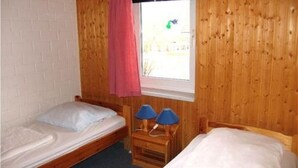 Une chambre avec deux lits simples, des murs en bois, une fenêtre avec un rideau et deux lampes de chevet.