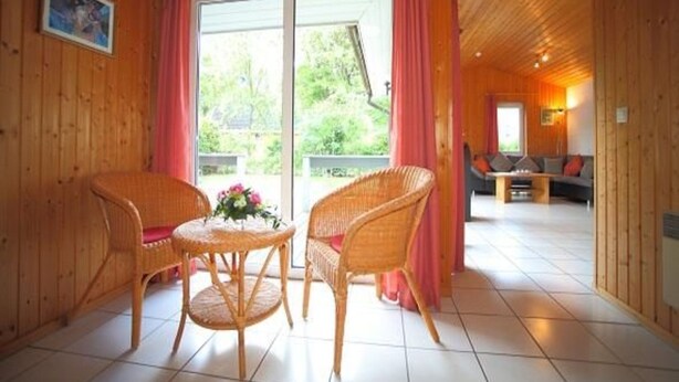 Un intérieur en bois avec des chaises et une table en osier, un canapé et une grande fenêtre avec des rideaux.