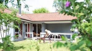 Une maison avec un toit recouvert de tuiles rouges, une véranda et une cour clôturée.