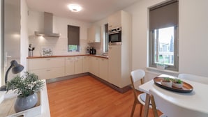 Eine moderne Küche mit weißen Schränken, einer Holzarbeitsplatte und einem eingebauten Backofen. Ein Esstisch mit Stühlen und ein Fenster mit Blick ins Freie sind ebenfalls vorhanden.