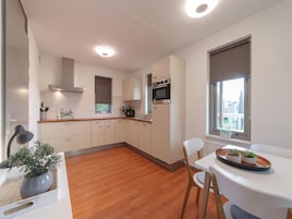 Una cocina moderna con armarios blancos, encimera de madera y horno empotrado. Hay una mesa de comedor con sillas y un ventanal con vistas al exterior.