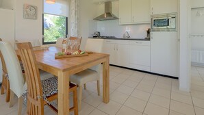 A modern kitchen with white cabinets, a wooden dining table with chairs, and a window with curtains. - Bungalow in Sondel Near Slotermeer Lake (Sondel)