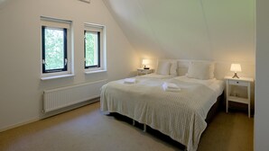 A bedroom with a sloped ceiling, two windows, a bed with white bedding, a bedside table with a lamp, and a radiator. - Bungalow in Sondel Near Slotermeer Lake (Sondel)
