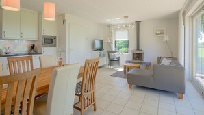 A modern kitchen with white cabinets, a dining table with chairs, a grey sofa, and a fireplace. - Bungalow in Sondel Near Slotermeer Lake (Sondel)