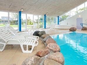 A swimming pool with white lounge chairs and large rocks, surrounded by large windows and a tiled floor. - 6 Person Holiday Home on a Holiday Park in Hemmet (Hemmet)