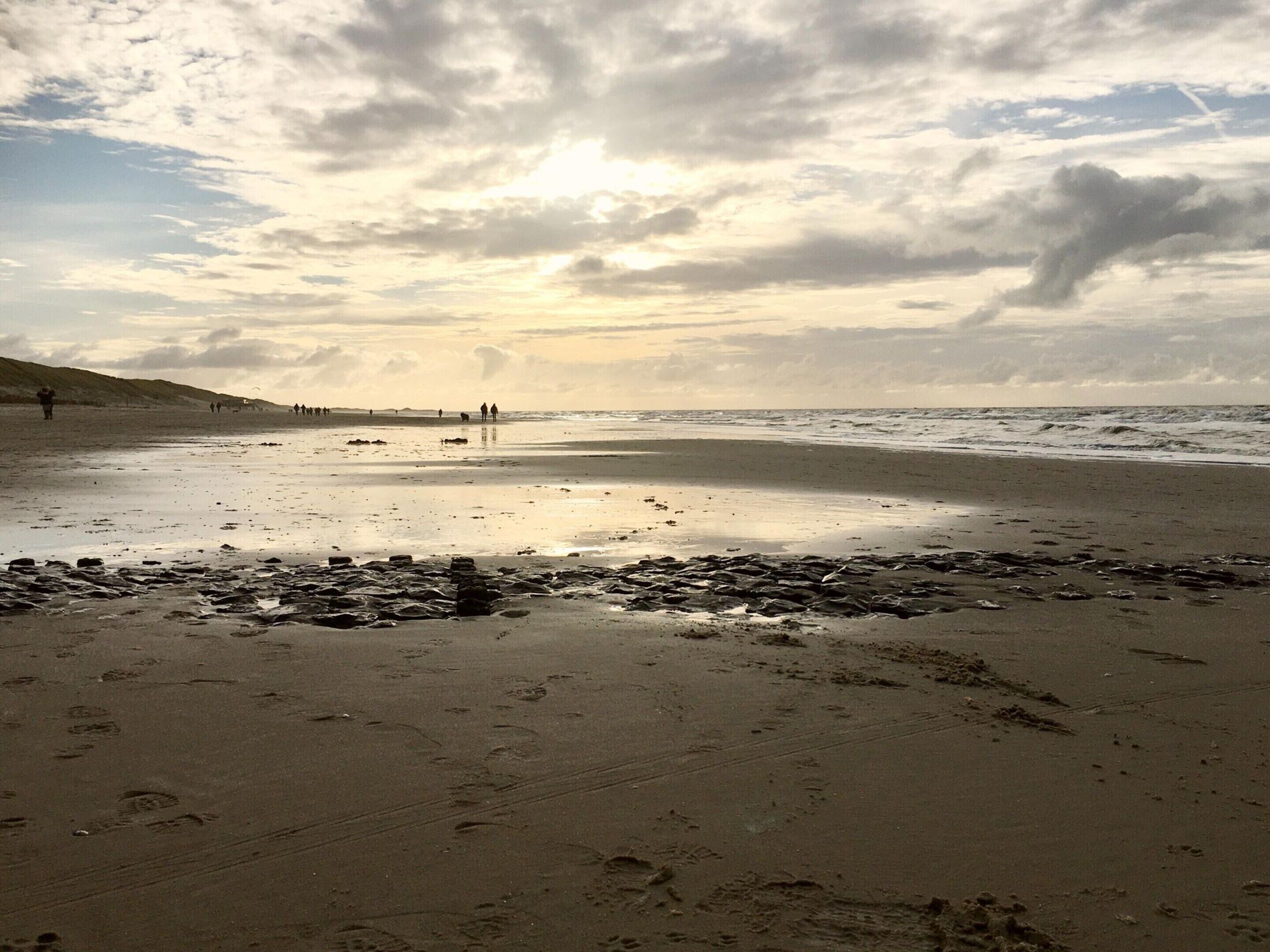 En strand med fotspår och stenar i förgrunden, en sandstrand och en molnig himmel.
