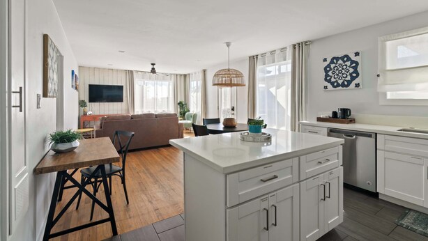 Une cuisine moderne avec des meubles blancs, un îlot central et un coin repas comprenant une table et des chaises en bois.