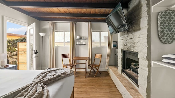 A cozy room with a bed, wooden floor, a fireplace, a TV mounted on the wall, and a table with chairs. - Boho Bungalow Studio Walk to Beach (San Diego)