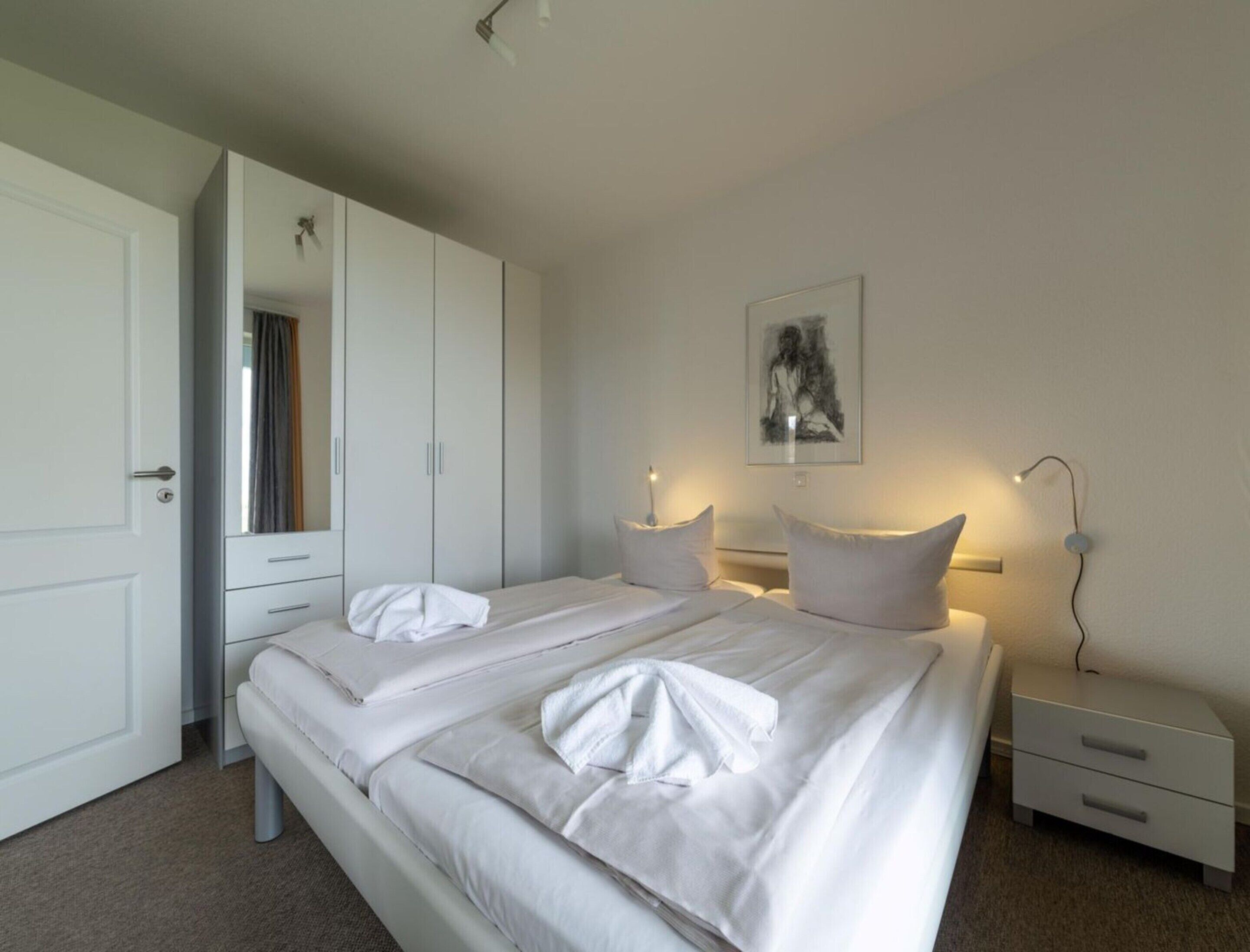 A bedroom with a double bed, two bedside tables, a wardrobe, and a framed picture on the wall.