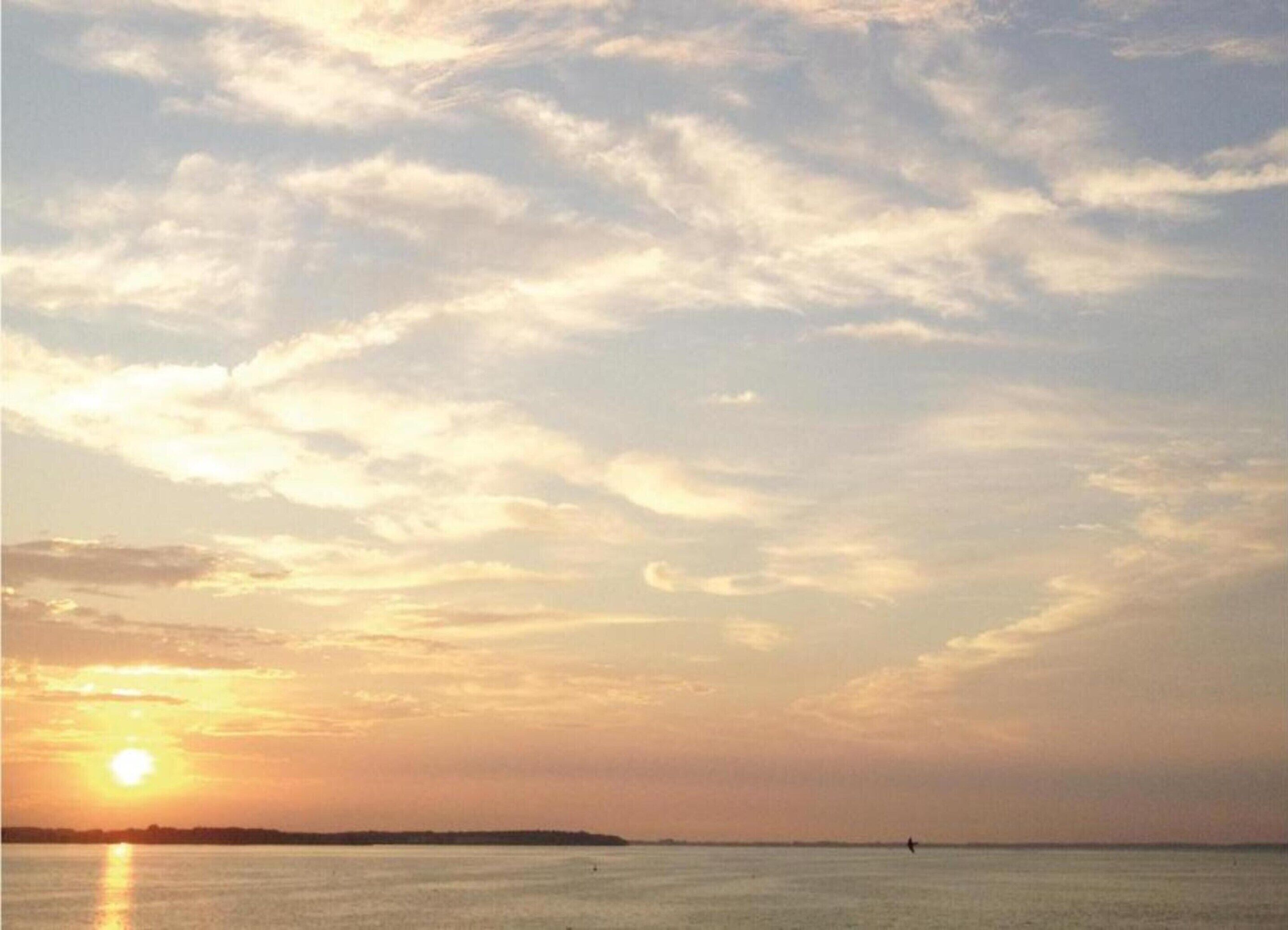 A sunset over a calm body of water with a distant shoreline.