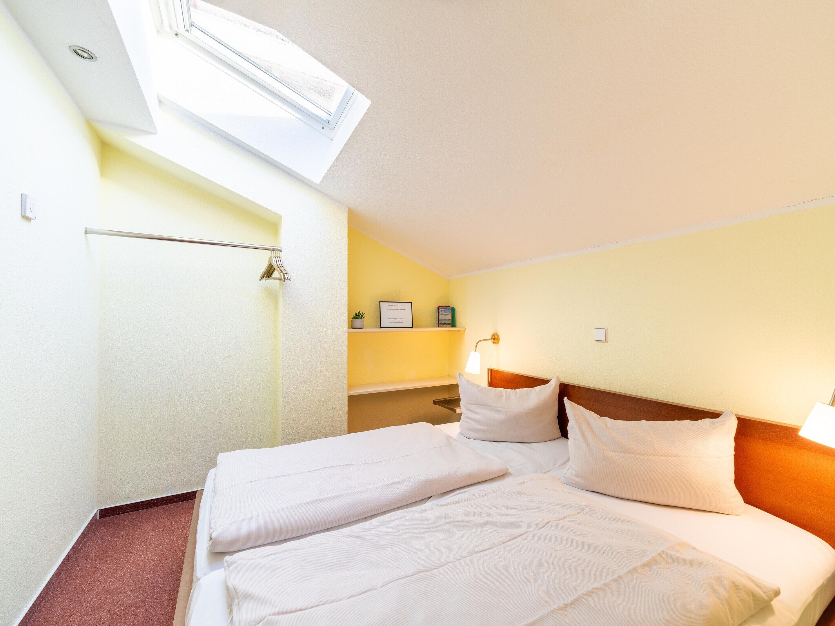 A hotel room with a bed, a bedside table, a lamp, a small plant, and a window.