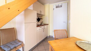 Una cocina compacta con una escalera de madera, una mesa de comedor y una silla de mimbre.