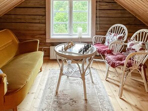 A cozy room with a wooden ceiling, a round table with chess pieces, a yellow sofa, and white chairs with red cushions. - 4 Person Holiday Home in Virserum (Virserum)