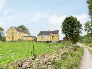 A rural setting with two yellow houses, a dirt path, and a grassy field. - 4 Person Holiday Home in Virserum (Virserum)
