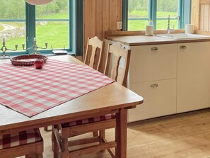 A kitchen with a wooden table, chairs, a checkered tablecloth, a window with a view of greenery, and a sink with a faucet. - 4 Person Holiday Home in Virserum (Virserum)