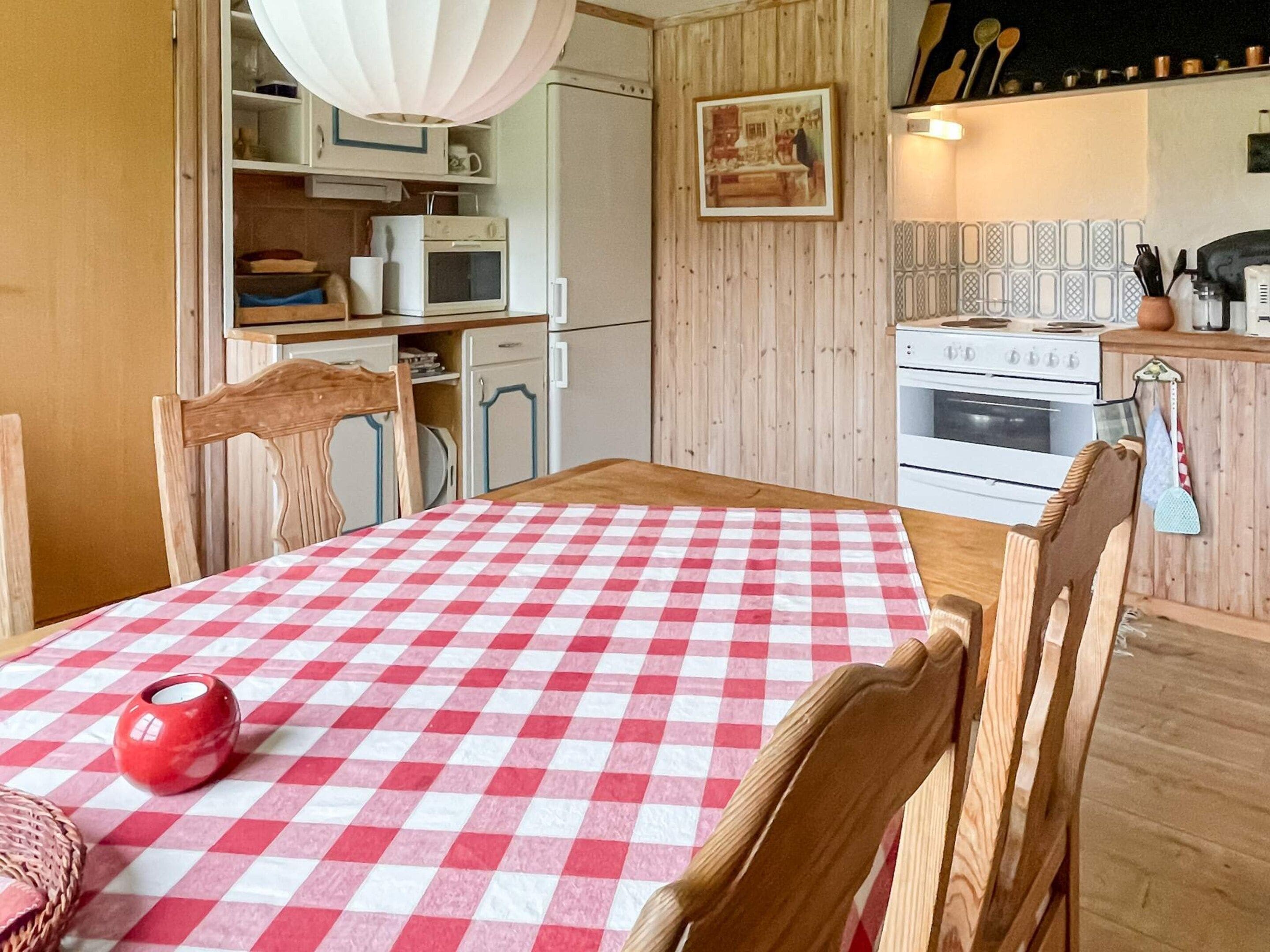 A kitchen with wooden cabinets, a microwave, an oven, and a dining table with a checkered tablecloth.