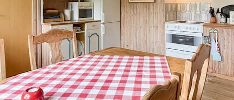 A kitchen with wooden cabinets, a microwave, an oven, and a dining table with a checkered tablecloth.