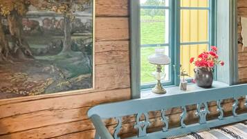 A room with a wooden bench, a painting, a window with a view of greenery, and a vase with flowers on the windowsill.