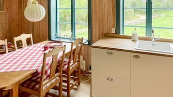 A kitchen with a wooden table and chairs, a white sink, and a window with a view of greenery.